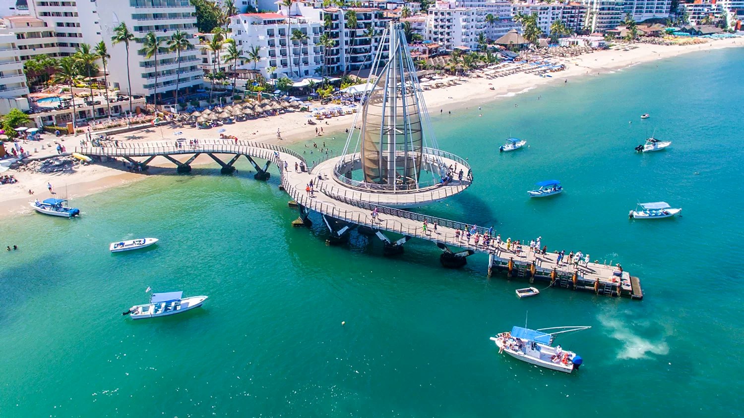 Vista aérea del muelle de Playa Los Muertos, con su vela de acero, lanchas en el agua turquesa y la playa con palapas